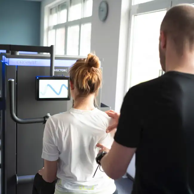 Gregor Mini kontrolliert und korrigiert die korrekte Ausführung einer Übung einer Patientin.